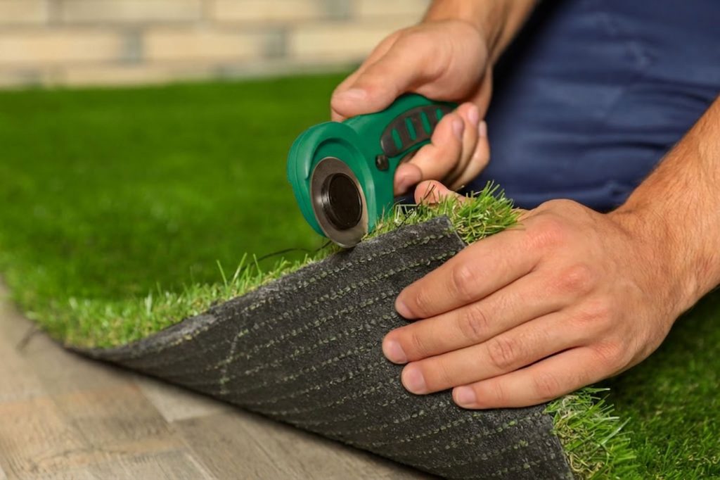 Close-up of a professional installer cutting and fitting artificial turf during a residential lawn installation project.
